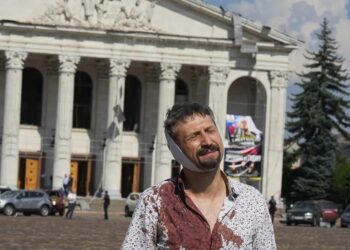 Homem ferido após bombardeio em Chernihiv, no norte da Ucrânia, com teatro da cidade também atingido ao fundo, em 19 de agosto de 2023. — Foto: Efrem Lukatsky/ Ap.