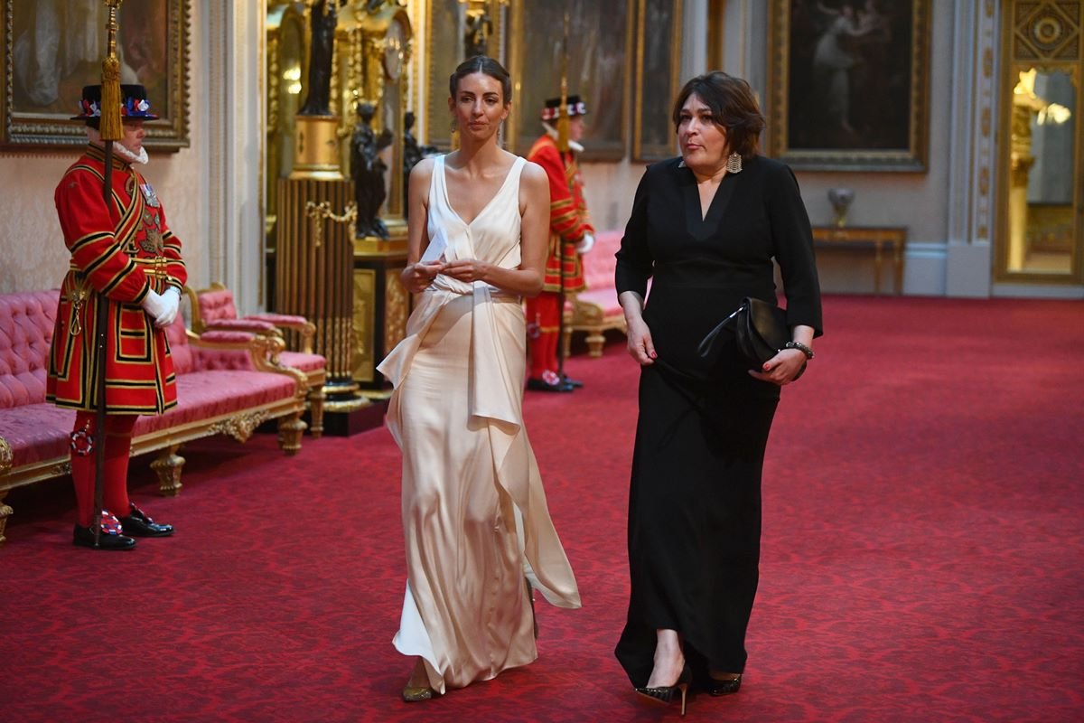 Rose Hanbury é uma mulher branca e elegante. Ela está usando um vestido branco de gala e caminha acompanhada de outra mulher vestida de preto - Metrópoles