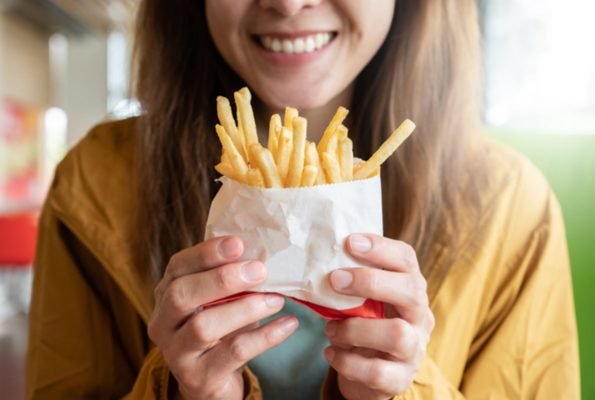 Imagem colorida de mulher com batata frita na mão