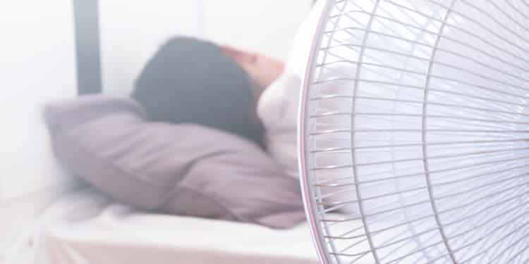 A man Sleeping on the bed and turn on the fan over the head risks of respiratory system.Health and medical care concepts