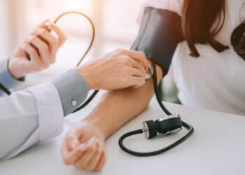 Doctor using sphygmomanometer with stethoscope checking blood pressure to a patient in the hospital.