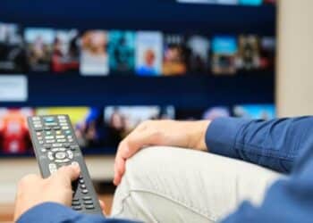 unrecognizable man sitting on the sofa with a remote control in his hand searching for content on a streaming platform