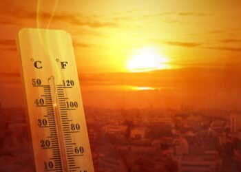 Thermometer with high temperature on the city with glowing sun background. Heatwave concept