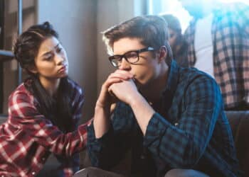 Young asian woman supporting male friend in depression, other people on background