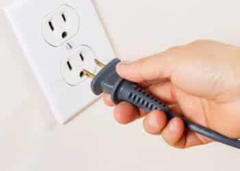Horizontal photo of female hand inserting power cord receptacle into electric wall outlet