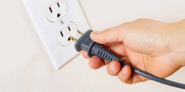 Horizontal photo of female hand inserting power cord receptacle into electric wall outlet