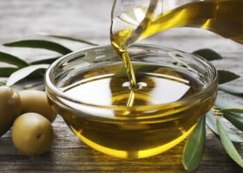 Bottle pouring virgin olive oil in a bowl close up
