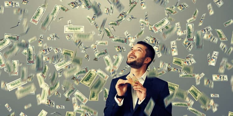 excited laughing businessman standing under dollar's rain, holding money and looking up