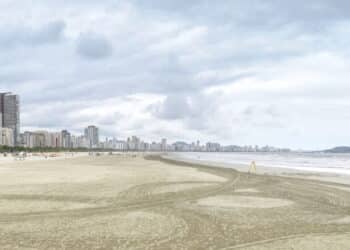 Panoramic view of a beach of Santos SP Brazil. Jose Menino beach. Long sand bank with sunshades, the sea and the city on background. Brazilian coastal city.