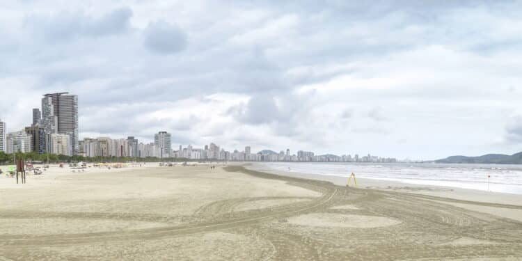 Panoramic view of a beach of Santos SP Brazil. Jose Menino beach. Long sand bank with sunshades, the sea and the city on background. Brazilian coastal city.