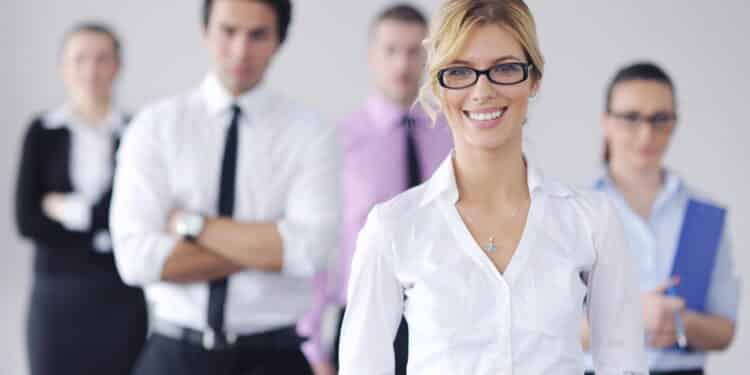 Successful business woman standing with her staff in background at modern bright office