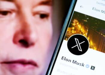 Elon Musks Twitter profile on a smartphone and Elon Musk in the background.