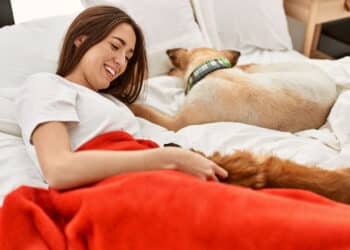 Young hispanic woman hugging dog lying on bed at bedroom