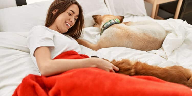 Young hispanic woman hugging dog lying on bed at bedroom