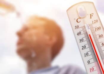 Man pouring water on his head in extreme heat. Thermometer in summer day shows or indicate high temperature degree with sun in background.