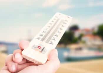 Hand holding thermometer on city with lake background as summer heat concept