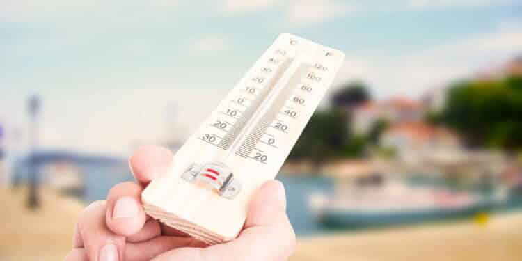 Hand holding thermometer on city with lake background as summer heat concept