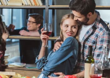 Two loving couples resting in room, one couple embrace at table and other sitting by bookshelf