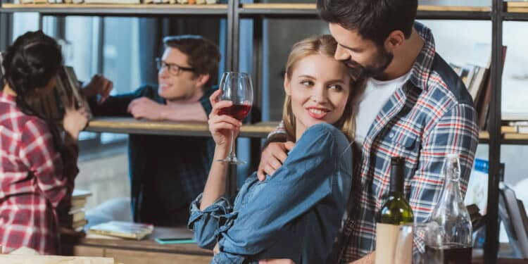 Two loving couples resting in room, one couple embrace at table and other sitting by bookshelf