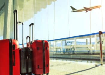 stack of traveling luggage in airport terminal and passenger plane flying over sky