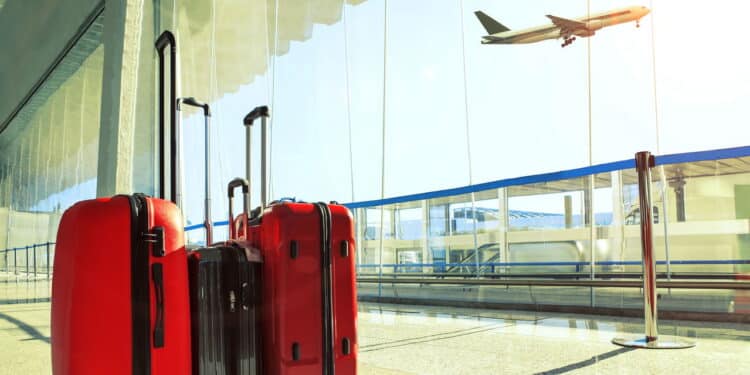 stack of traveling luggage in airport terminal and passenger plane flying over sky