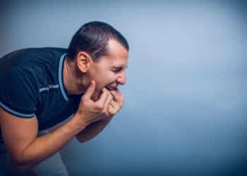 the man of European appearance brunet shoved his fingers in his mouth on a gray background cross process