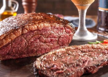 Grilled sliced cap rump steak with two glasses of beer on wooden cutting board. Marble meat beef (Brazilian picanha).