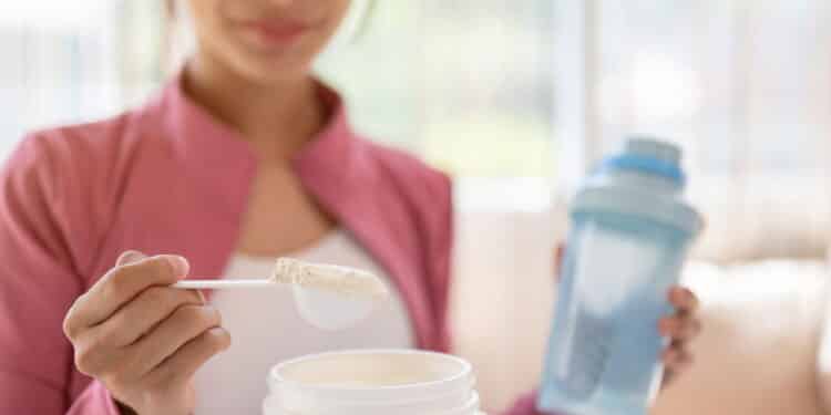 Close-up image of a healthy and fit Asian woman in sportswear making her protein shake after a workout at home. Drink supplements, high-nutrition drinks, diet, and muscle-building