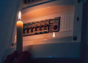 Energy crisis. Hand in complete darkness holding a candle to investigate a home fuse box during a power outage. Blackout concept.