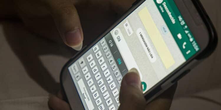 female hands typing a message in Portuguese ( hello ) in a messaging application on a white cell phone in Rio de Janeiro.