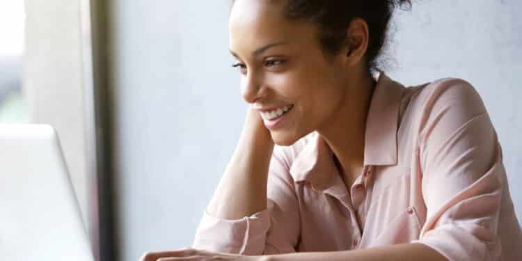 Close up portrait of a beautiful young woman smiling and looking at laptop screen