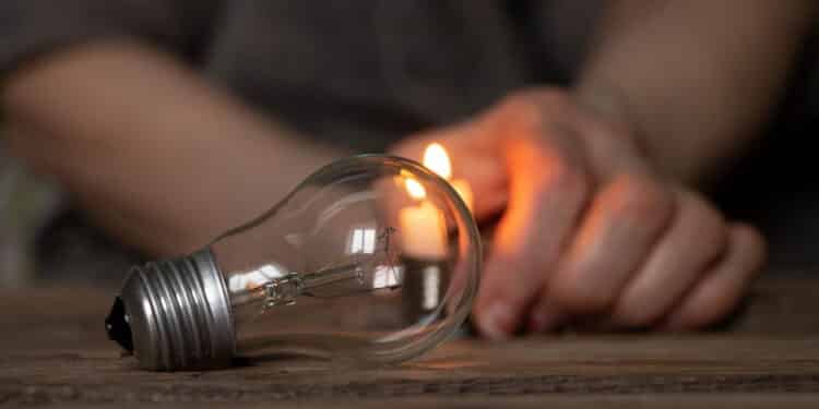 An incandescent light bulb and a candle in the hands of an old woman on a wooden table, people without light, the light of a candle when there is no light in Ukraine