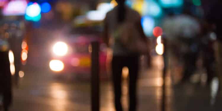 An blurred, out of focus street prostitute waits for customers as cars slowly cruise by in the Silom district of Bangkok, Thailand