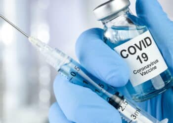 Healthcare cure concept with a hand in blue medical gloves holding Coronavirus, Covid 19 virus, vaccine vial