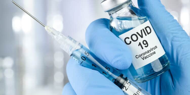 Healthcare cure concept with a hand in blue medical gloves holding Coronavirus, Covid 19 virus, vaccine vial