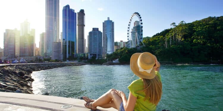 Holidays in Brazil. Attractive young woman enjoying sunset sitting on promenade in Balneario Camboriu, Santa Catarina, Brazil.