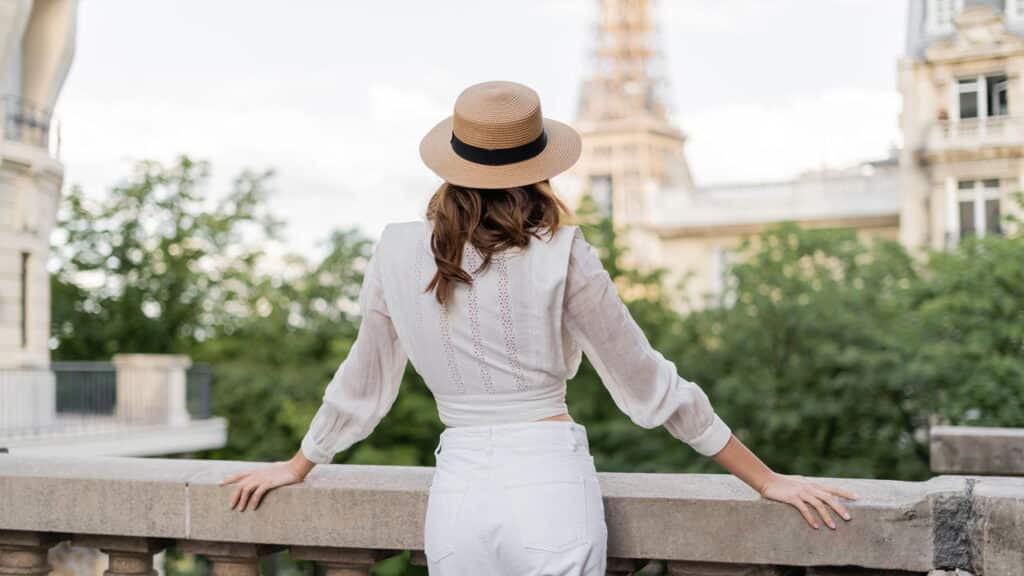 vista de turista com chapéu de sol em pé com a Torre Eiffel desfocada ao fundo em Paris