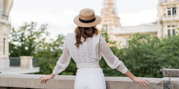 vista de turista com chapéu de sol em pé com a Torre Eiffel desfocada ao fundo em Paris