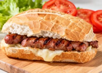 Pão com linguiça e queijo e ao fundo alface e tomate