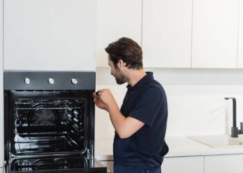 Técnico realizando manutenção em forno embutido (Créditos: depositphotos.com / IgorVetushko)