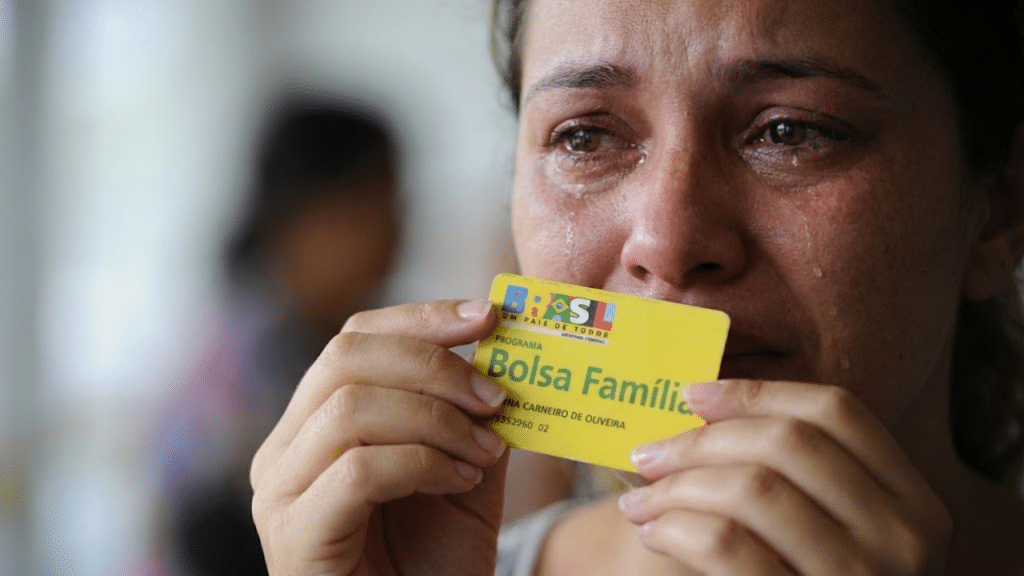 Mulher chorando com cartão do Bolsa Família na mão