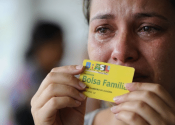 Mulher chorando com cartão do Bolsa Família na mão