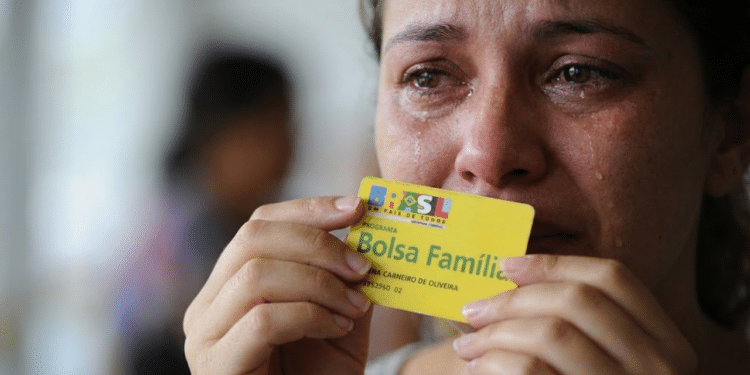 Mulher chorando com cartão do Bolsa Família na mão