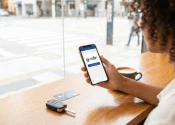 Pessoa no café ativando o cadastro no celular, com chave do carro e cartão de crédito na mesa