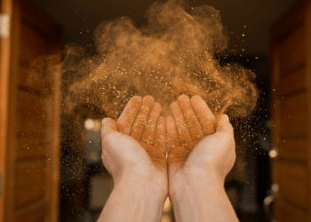 Close mágico de mãos soprando canela e purpurina dourada para dentro de uma porta iluminada pelo sol