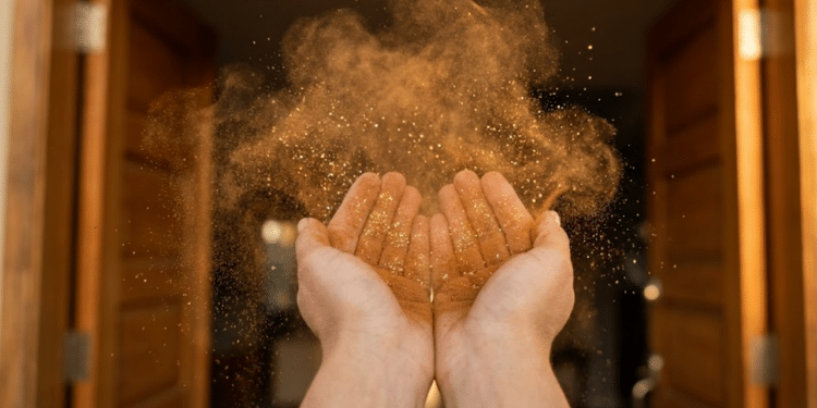 Close mágico de mãos soprando canela e purpurina dourada para dentro de uma porta iluminada pelo sol