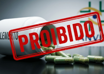 Frasco de suplemento derramando cápsulas verdes na mesa com um carimbo vermelho de 'PROIBIDO' por cima