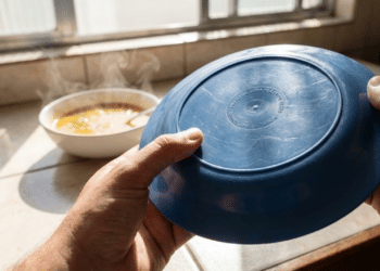 Mão inspecionando fundo de prato plástico sob luz solar forte