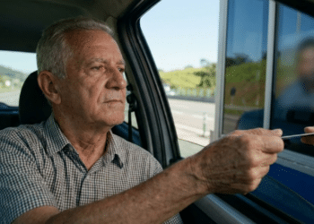 Idoso dentro do carro pagando a tarifa na cabine de pedágio em um dia ensolarado