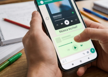Visão em primeira pessoa de um polegar digitando uma mensagem empolgada no chat verde do aplicativo de música sobre uma mesa de estudos
